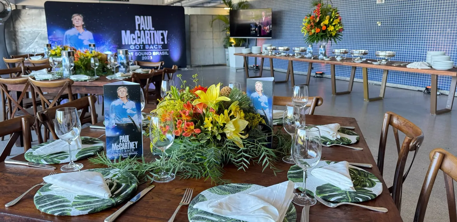 Mesa posta com arranjo floral e buffet ao fundo, no catering do show Paul McCartney Got Back.