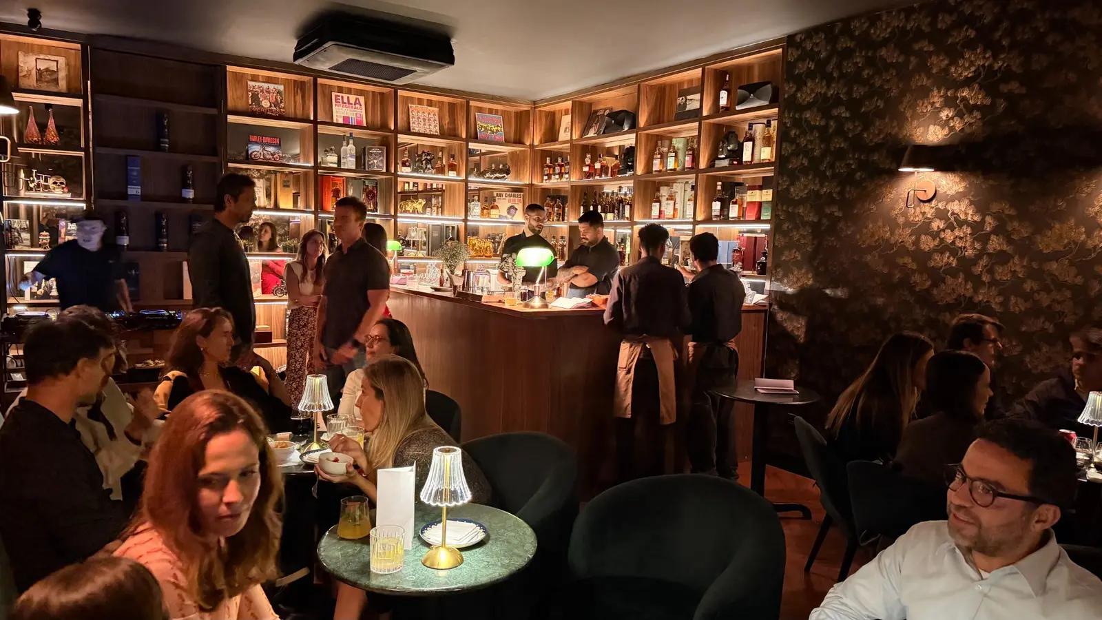 Interior do Âmbar Speakeasy em funcionamento, com bar, equipe e clientes.